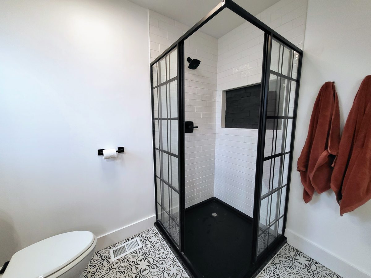 White subway tile shower with black-framed glass enclosure, black pan, and stacked-stone niche