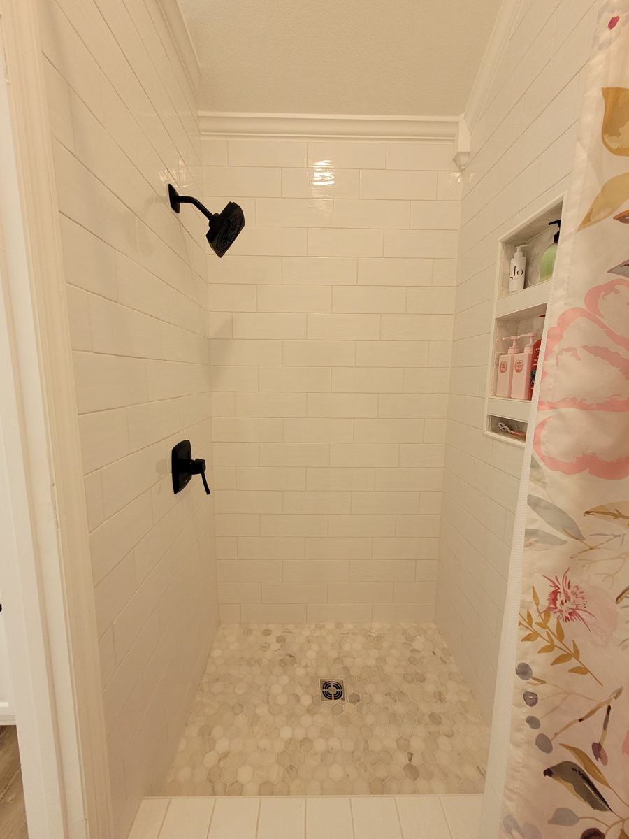 White subway tile shower with black fixtures, marble hex tile pan, and recessed niche