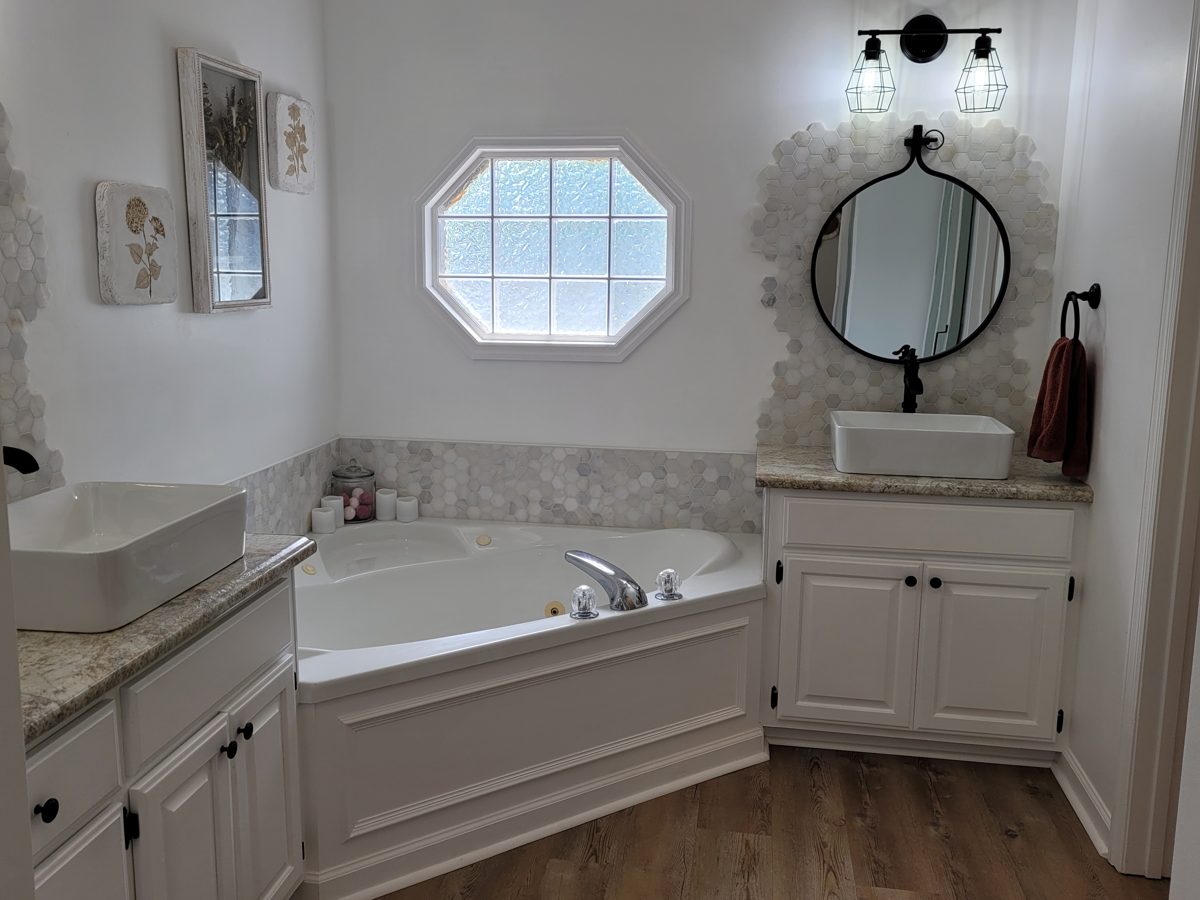 Marble hex tile tub surround and vanity backsplash in a white bathroom with black fixtures